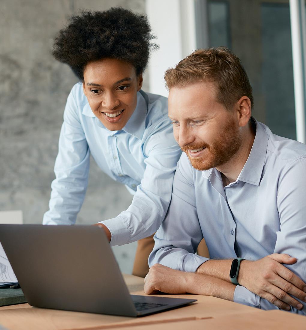 Professionally dressed coworkers looking at a laptop screen while smiling.