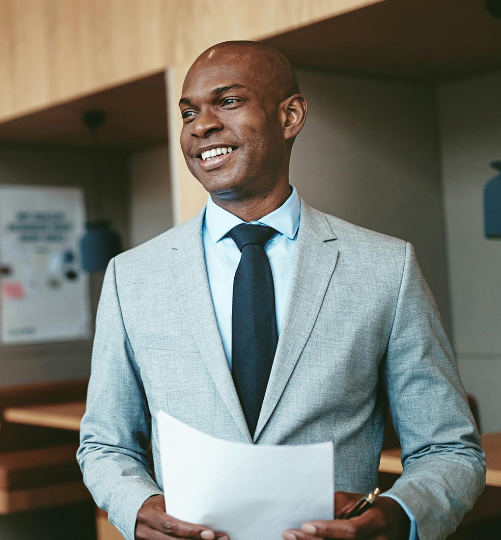 A smiling man in a suit holding important documents.